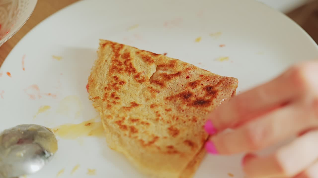 Delicious breakfast bite lifted by young woman’s hand with pink nails, Crepes