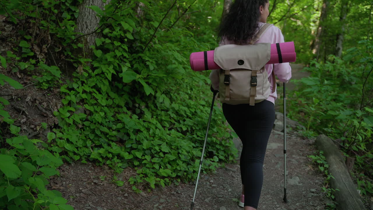 여성 이 숲 에서 배 과 트레킹 막대기 를 들고 산책 하고 있다