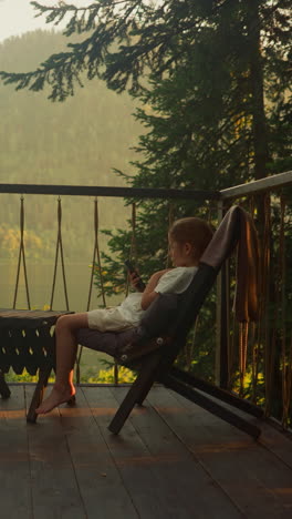 peers sit at table entertaining with smartphones. preschoolers use devices sitting on balcony in sunny summer weather. video depicts ambiance for unwinding