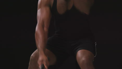 toma de estudio de cerca de un atleta masculino entrenando en un chaleco de fitness usando cuerdas de batalla tomada contra un fondo negro
