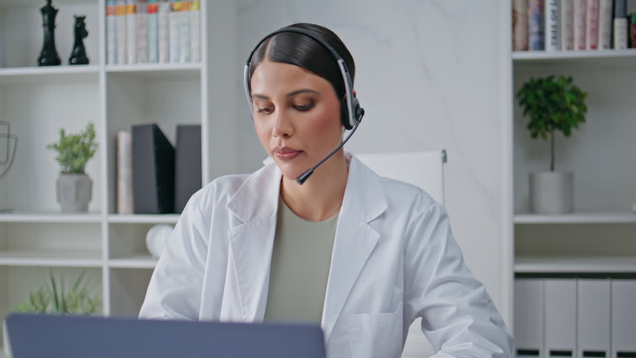 Primer plano de una doctora con auriculares hablando por videollamada en un portátil en la oficina. Terapeuta hablando