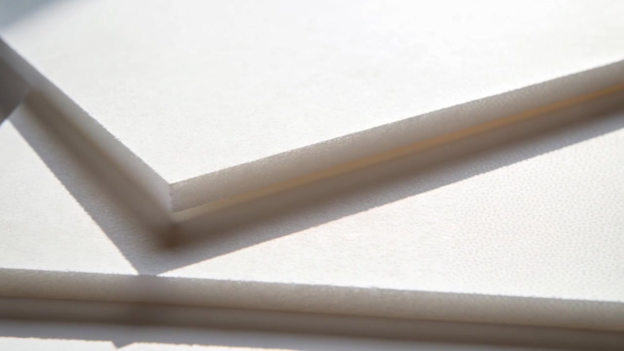 Moving camera framing stacked white sheets on table, bringing edges into view and shifting shadow
