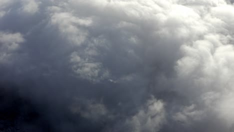 Dramatic-thick-clouds-over-mountaintops,-aerial-view-above-clouds