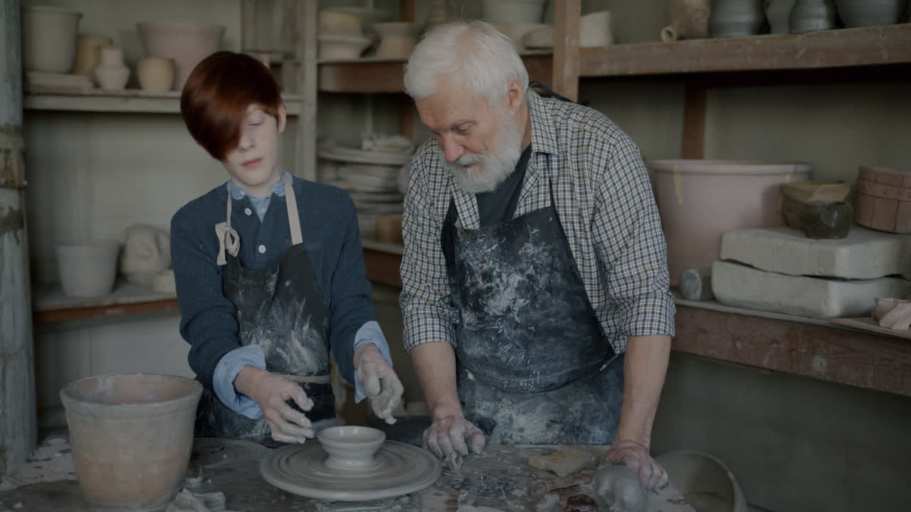 Young apprentice learning pottery from a senior master