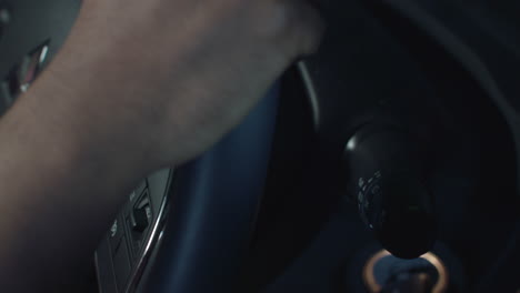 a driver reaches down from the steering wheel to hit the turn signal on a car with black interior