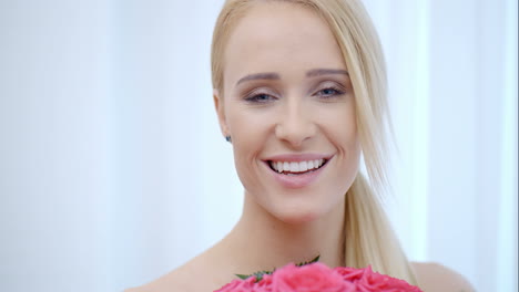 smiling blond woman smelling pink roses