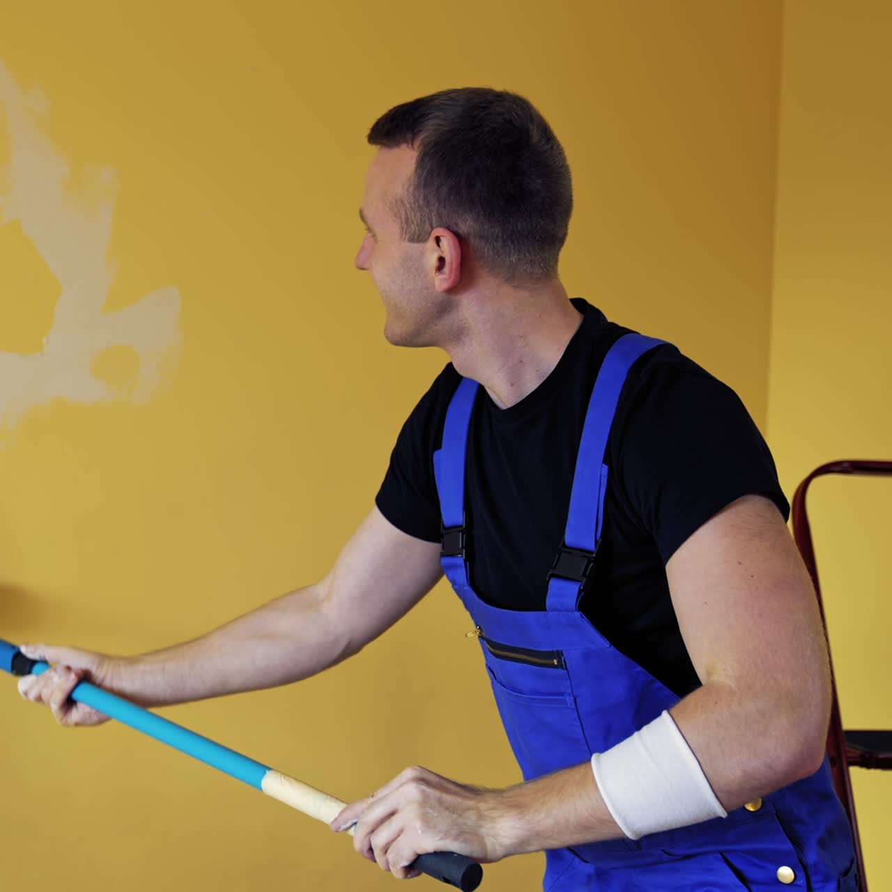Uomo che dipinge un cuore su un muro durante la ristrutturazione di un appartamento. Pittore che ritocca la parete di una stanza con il rullo su un manico lungo. Riparazione domestica.