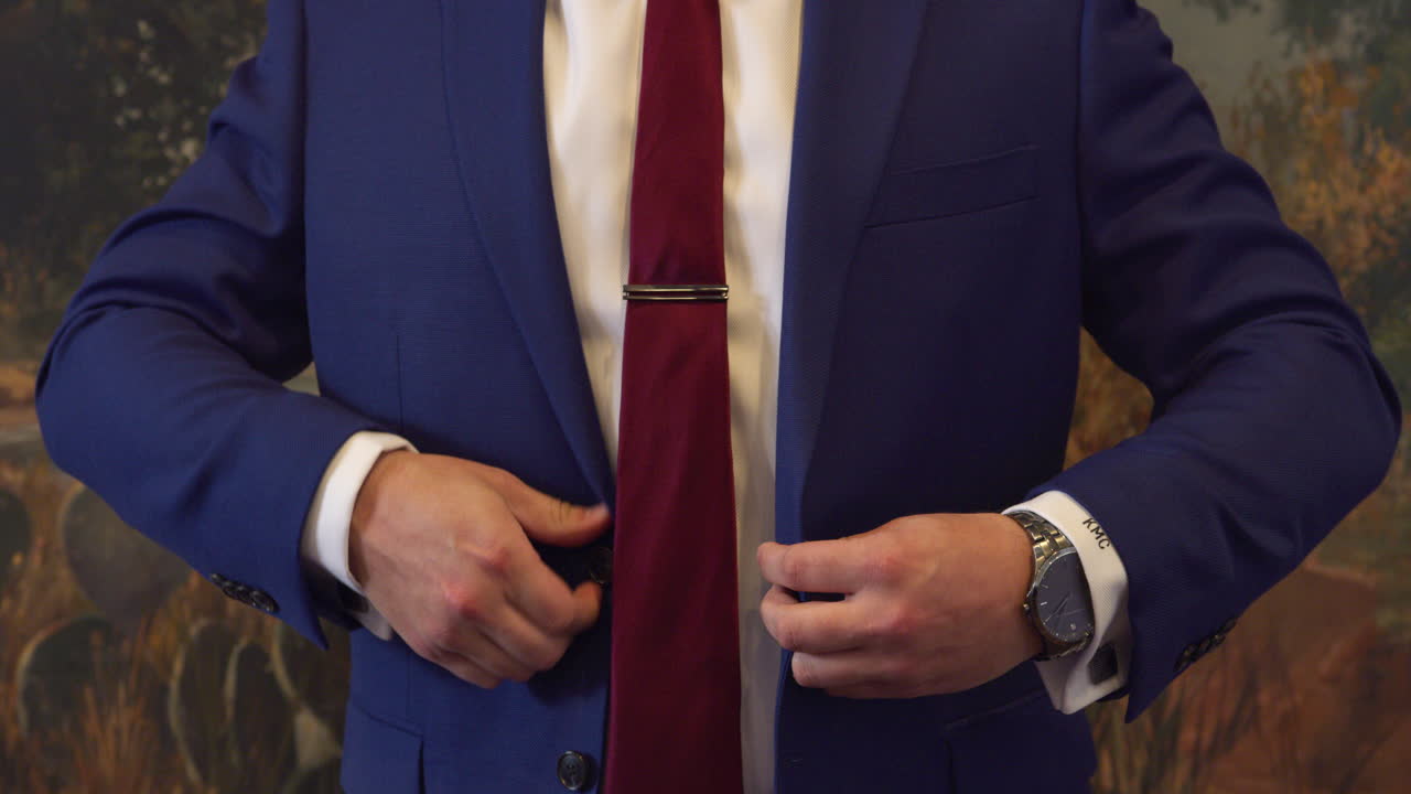 el novio preparándose para la boda y cerrando su chaqueta de traje azul con corbata