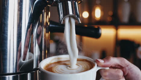 pouring frothed milk into a coffee cup