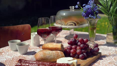 set-table-with-red-wine,-sausages-and-baguette-in-a-sunny-garden,-dolly-in