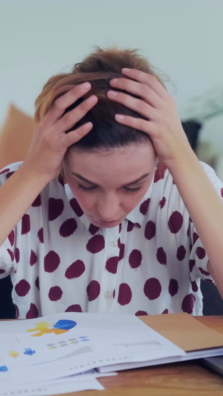 Mulher massageando as têmporas na mesa com relatórios financeiros