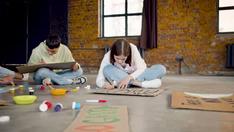 jóvenes activistas ambientales pintando carteles sentados en el suelo