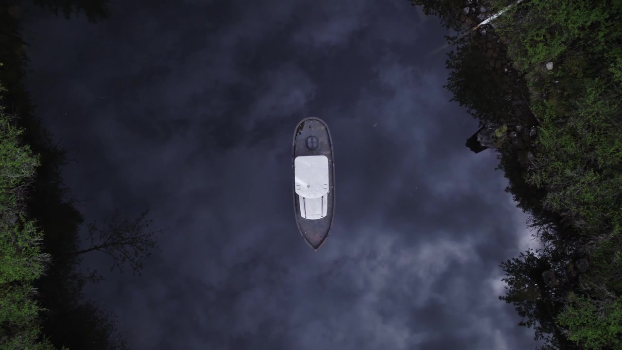 birdseye view of an old boat in the middle of a swampy, dark river
