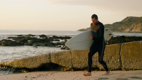 side view of mid-adult caucasian male surfer walking with surfboard at the beach 4k