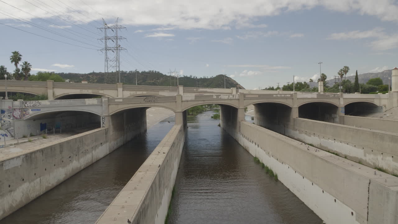 Metraje cinematográfico diurno 4K de 10 bits capturando una estructura de puente acueducto que atraviesa el corredor del río Los Ángeles. La toma destaca la geometría industrial del cruce y el río circundante.