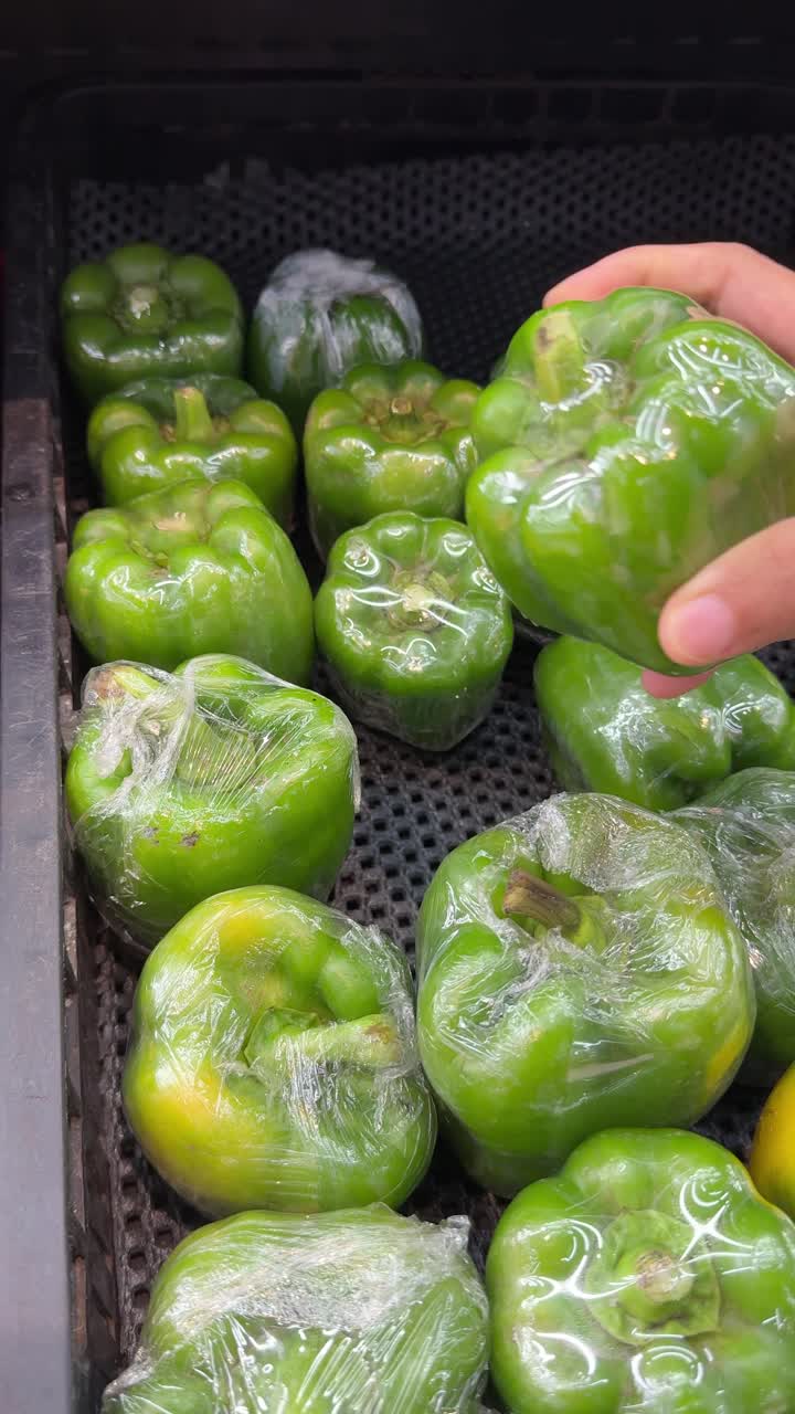 Handmatig selecteren van verse groene paprika in een supermarkt.