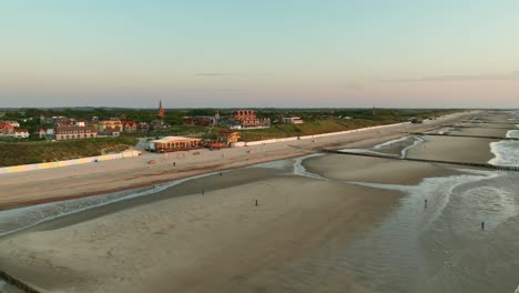Beautiful-aerial-shot-of-a-beach-at-low-tide-and-a-small-picturesque-coastal-town-during-golden-hour-on-a-cloudless-day