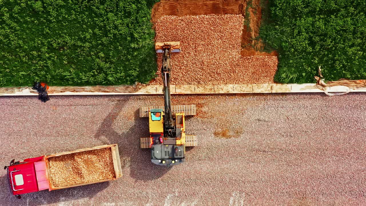 Excavator Spreading Gravel and Breakstone on Railway Construction Slope with Dumper Truck Nearby