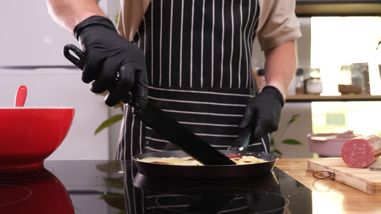 Un uomo versa uova sbattute in una padella con fette di salsiccia.