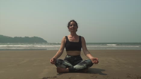 mujer joven en forma practicando una pose fácil de yoga, sukhasana, en una cálida playa tropical