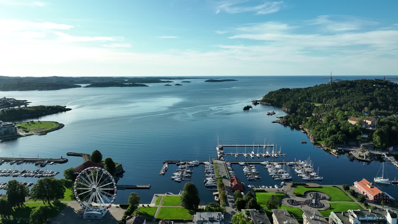 A stunning coastal landscape showcases a lively harbor with a prominent ferris wheel in Kristiansand