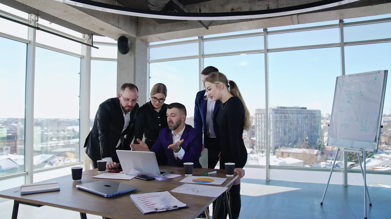 Teammates gathered around their boss to work out solutions. Chief sitting at the laptop and employees standing around and suggesting ideas.