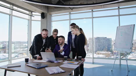 teammates gathered around their boss to work out solutions. chief sitting at the laptop and employees standing around and suggesting ideas.