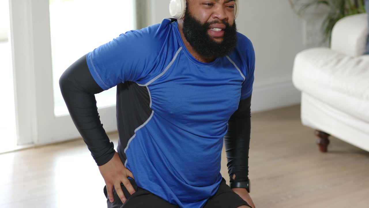 African American man starting workout at home kneeling on mat pushing up hips wearing headset