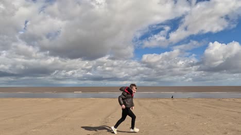 Young-boy-walking-along-a-wall-on-the-seafront-by-the-beach-on-a-stormy-sunny-day