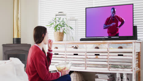 caucasian woman watching tv with african american male rugby player catching ball on screen