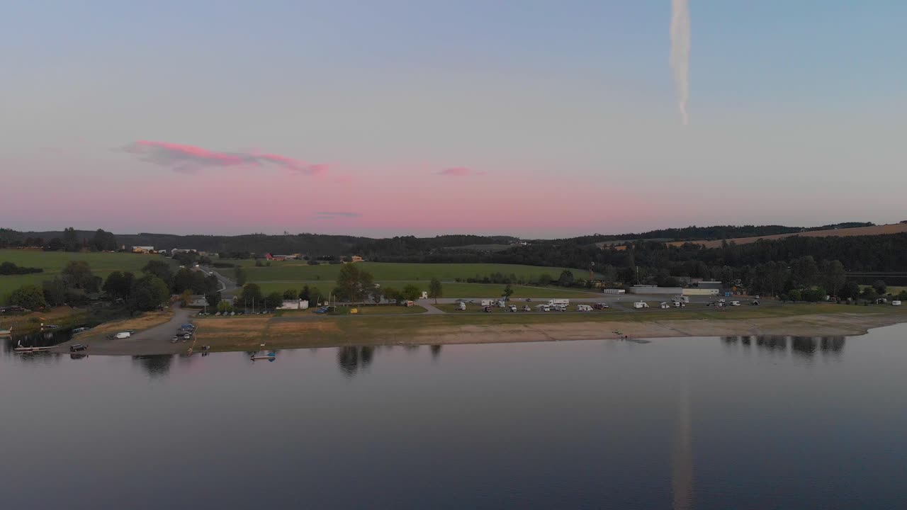 un vuelo aéreo de aspecto profesional hacia un campamento alemán en un tranquilo lago especular mientras el cálido atardecer