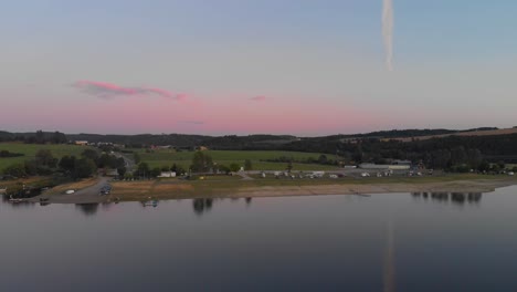 a professional looking aerial fyling towards a german campground at calm specular lake while warm sunset