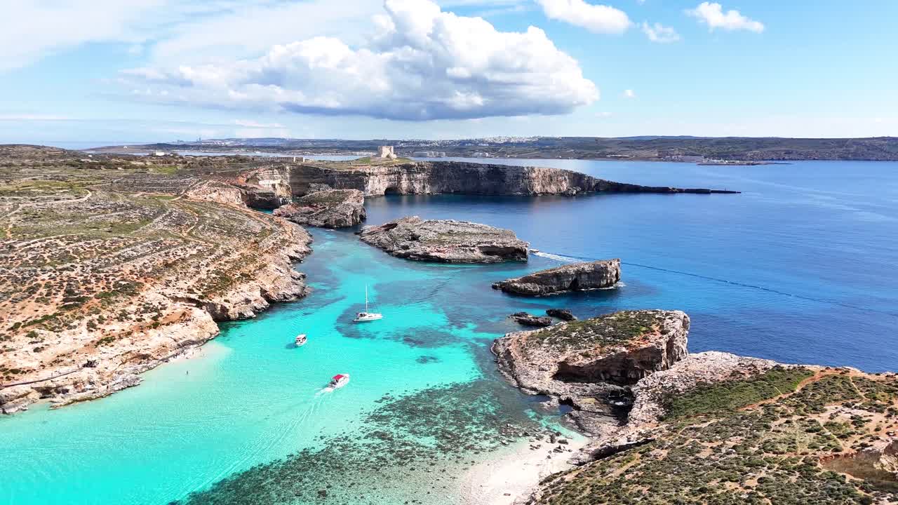 Luftfoto av Den blå lagune i Comino, Malta, med små båter på lyst turkist vann, steinete kystlinje og rolig sjø under en stor sky i dagslys.