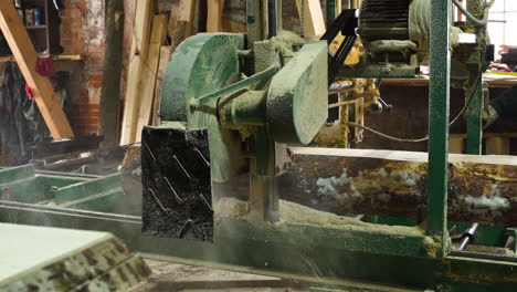 sawing log on electric stationary bandsaw in a sawmill, man pushing band saw