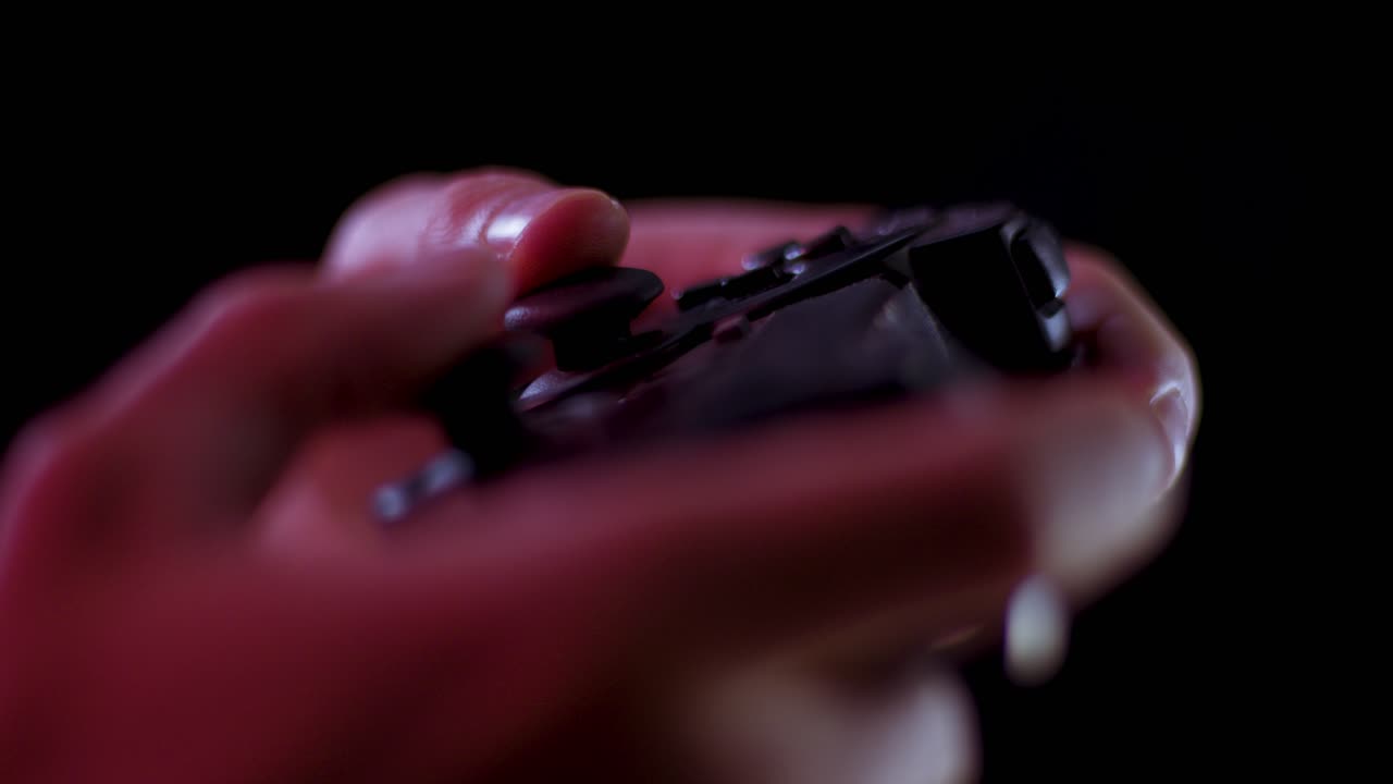 Playing video games in a darkened room with a black background close up on a small controller joystick playing slowly soft focus