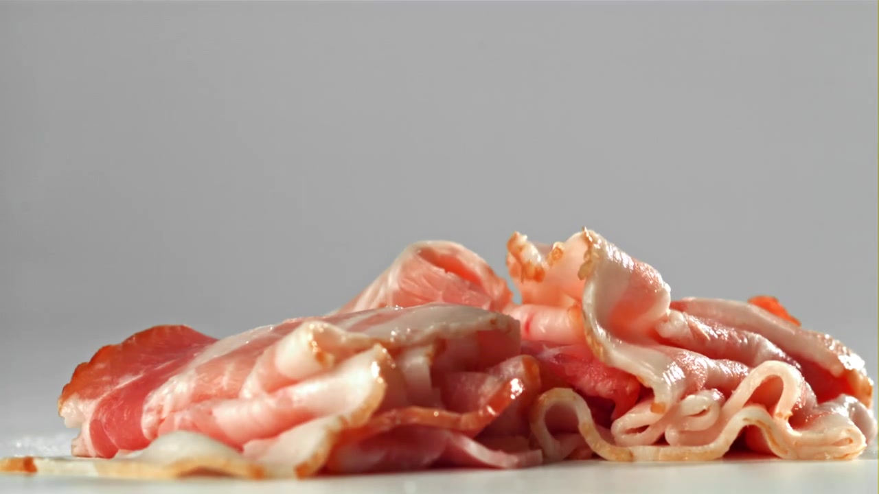 Fette di pancetta cruda che cadono al rallentatore