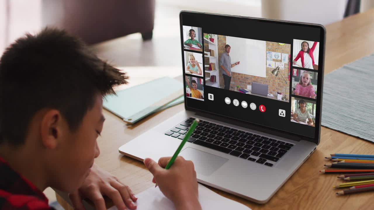 Schoolboy using laptop for online lesson at home, with diverse teacher and class on screen