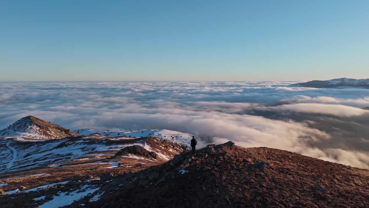 Person on mountain at sunrise with expansive clouds below
