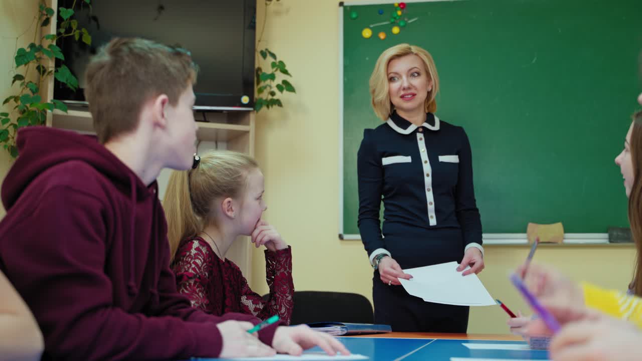 Back to school. Beautiful teacher talking with school children on the background of blackboard. Student asking questions to the teacher in the classroom.