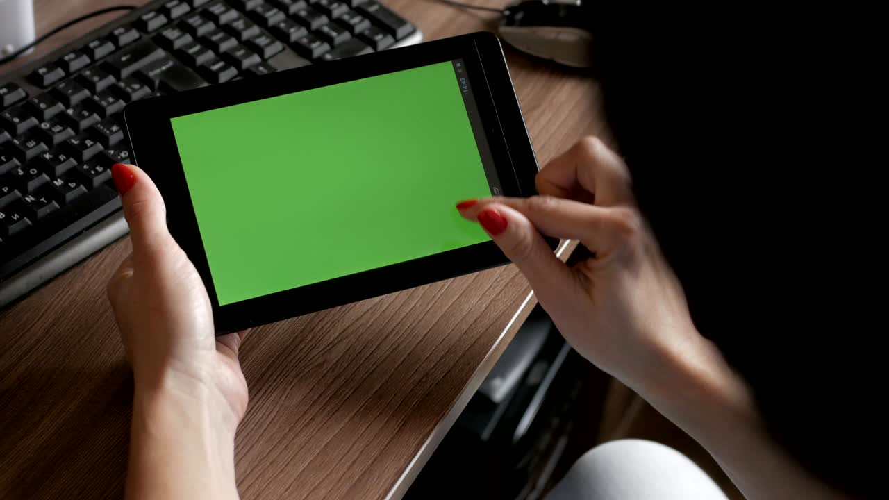 Woman in workplace using his digital tablet with green screen. Female hands using tablet mobile with empty green screen top view  work desk.  Technology scrollig tapping touchscreen business.