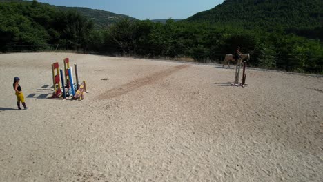 pullback drone shot reveals a trainer in the middle of the arena teaching two women how to ride a horse