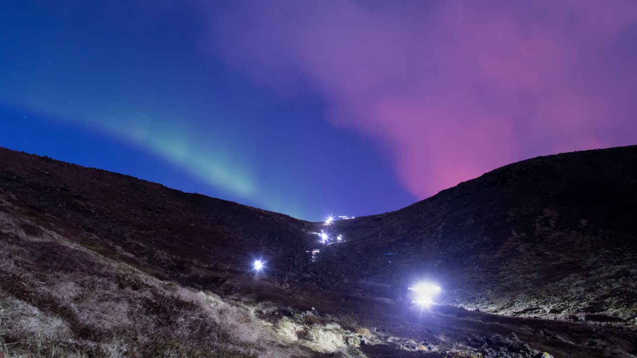la aurora boreal y el volcán brillan sobre las lámparas delanteras de los excursionistas que descienden