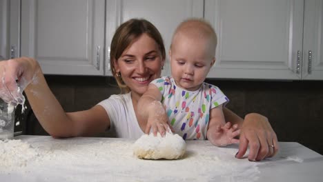 Young-mother-and-her-little-daughter-preparing-dough-on-the-table.-Baker-prepares-the-dough.-Family-girls-having-fun.-Slow-Motion