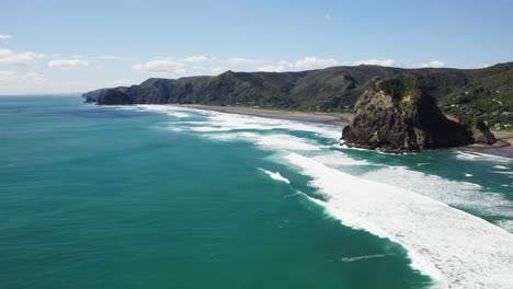 Looking-along-the-rugged-coastline-Piha-Beach,-at-the-famous-outcrop-known-as-Lion-Rock,-in-New-Zealand