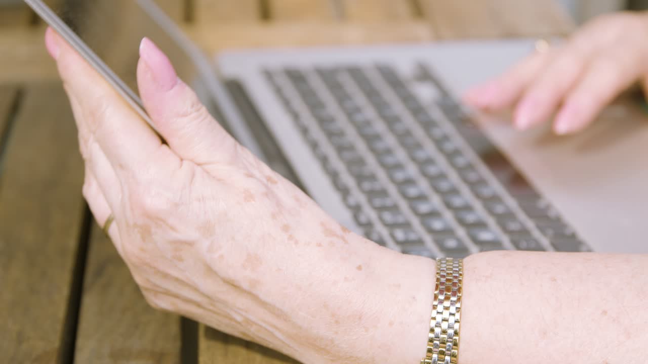 cierre las manos de una anciana mientras sostiene una pantalla de computadora portátil y se desplaza en el trackpad