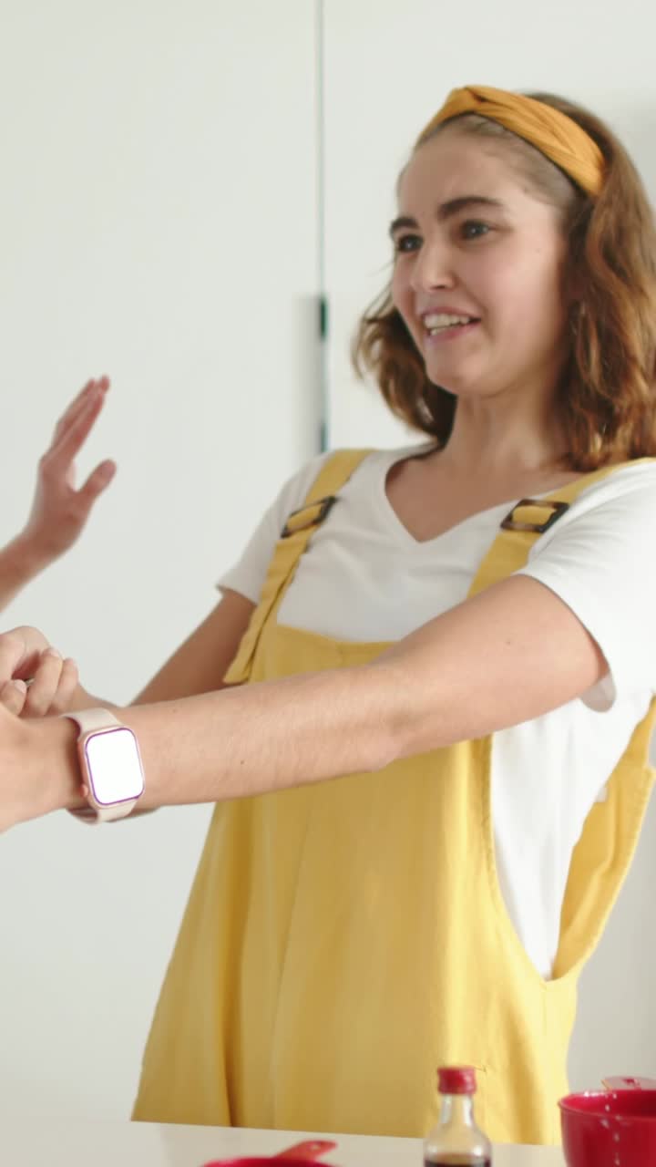 Video verticale: Una mano entra, donna in salopette gialla che mostra uno smartwatch e si appoggia al bancone