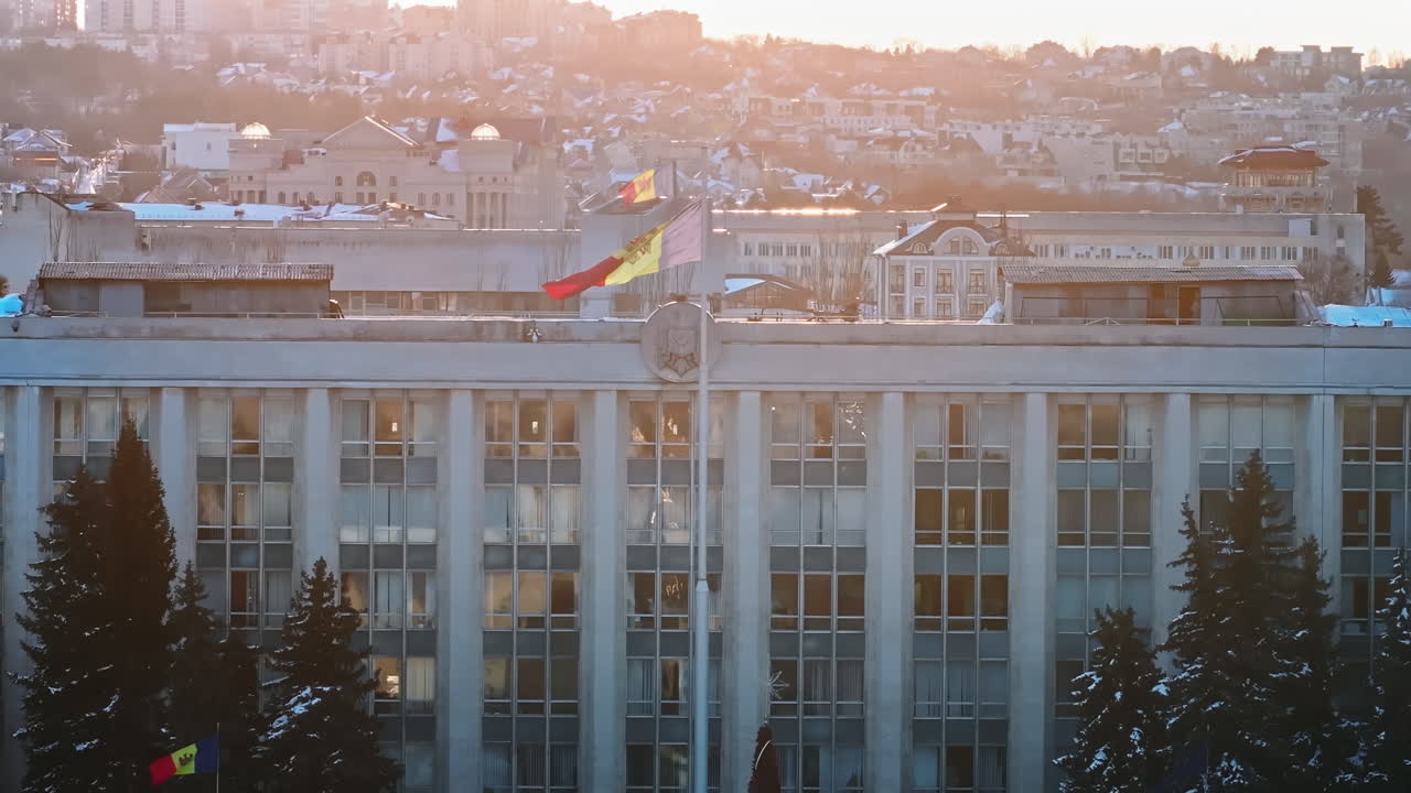 Aerial drone view of Moldova national flag and the Government House at sunset. Golden crosses on top of the Bell tower and the Metropolitan Cathedral of Christ's Nativity in foreground. Snowy Chisinau