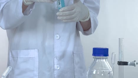 a lab technician carefully handles a blue liquid in a test tube using gloves.
