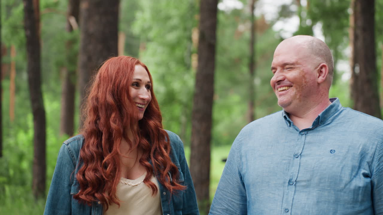 Ein glückliches Paar in passenden blauen Outfits geht gemeinsam durch einen üppigen Wald, hält Händchen und lächelt warmherzig, umgeben von grüner Natur und sanftem Sonnenlicht und drückt Liebe, Frieden und Verbundenheit aus.
