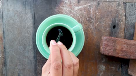 vista superior mujer mano agitar negro luwak balí café con mesa de madera y vaso de taza verde sentirse feliz y lleno de energía por la mañana
